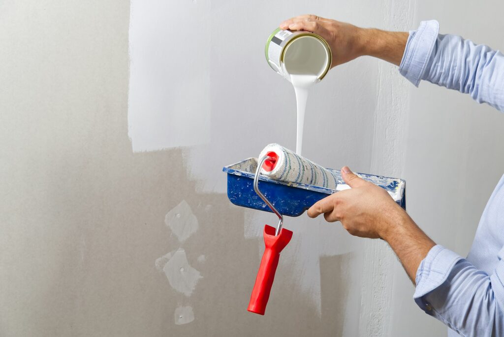 Men hand painting wall with paint roller with white color. Painting apartment, renovating concept